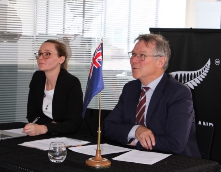 An image of David Parker and Alison Hamilton sitting at a desk with an NZ flag ornament prominently set on the table in front of them..