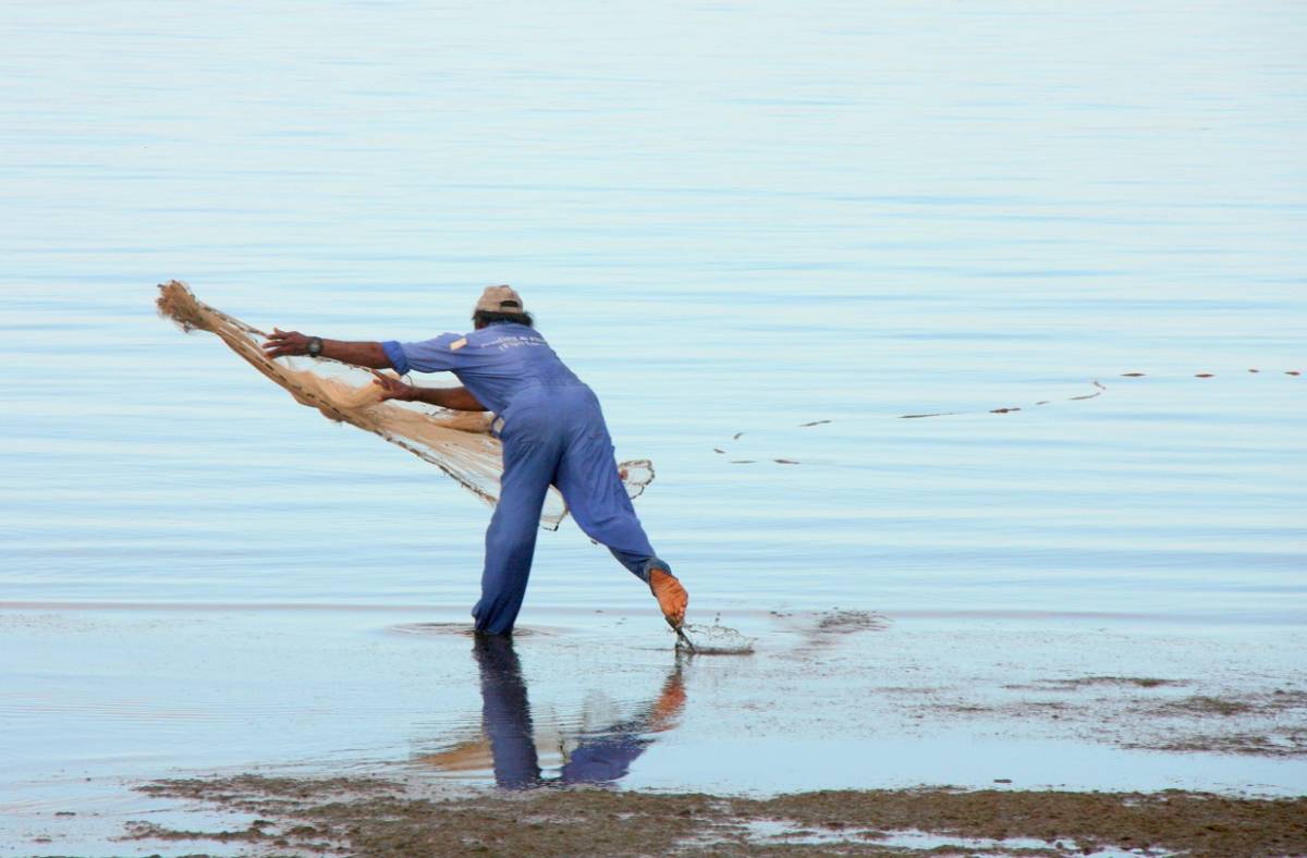 An image of a man throwing a fishing net into the sea. 