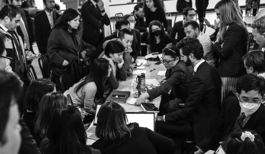 Several delegates huddle around President of the Conference, Singapore’s Rena Lee. 