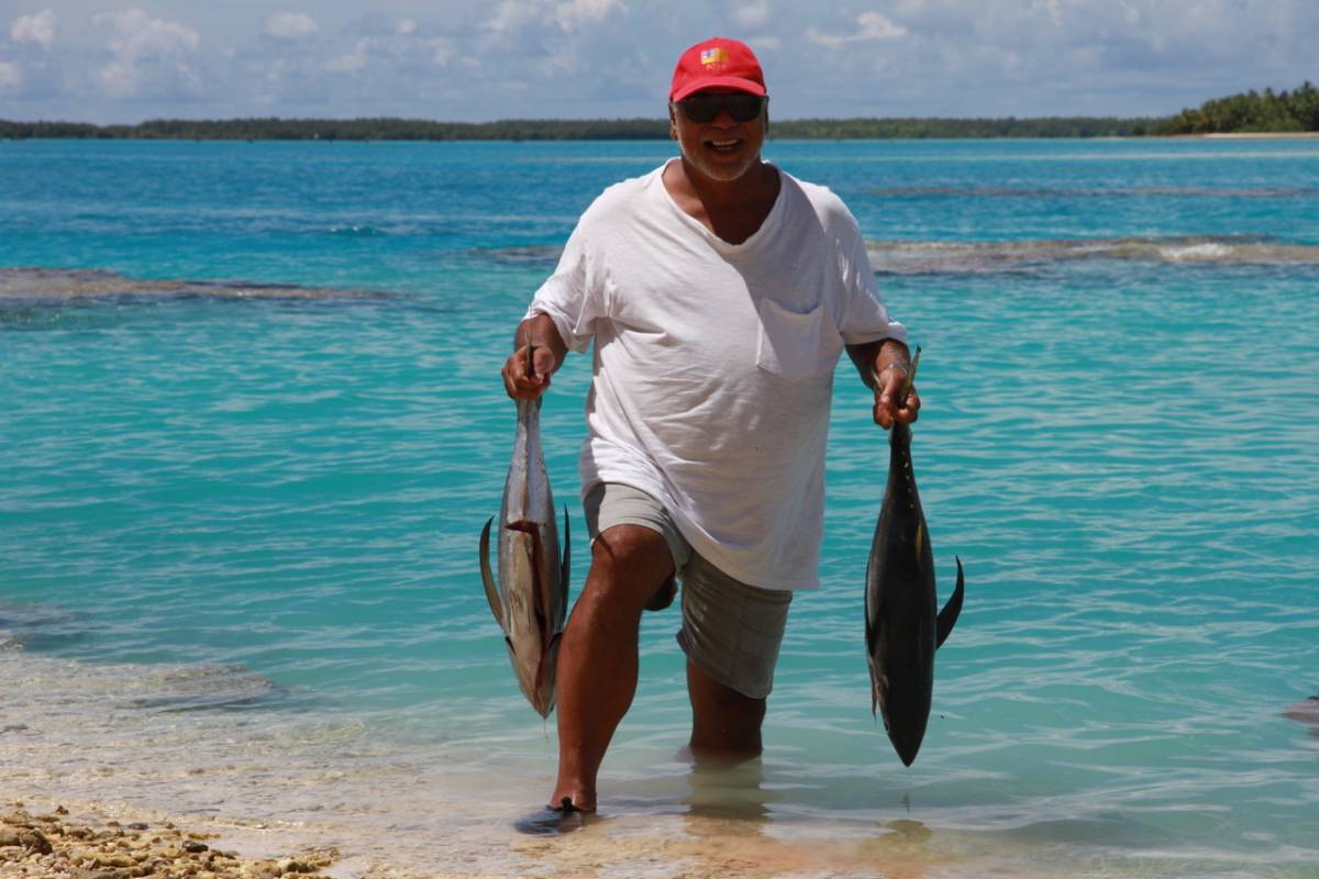 An image of a person standing in the shallows of the sea holding a large fish in each hand. .