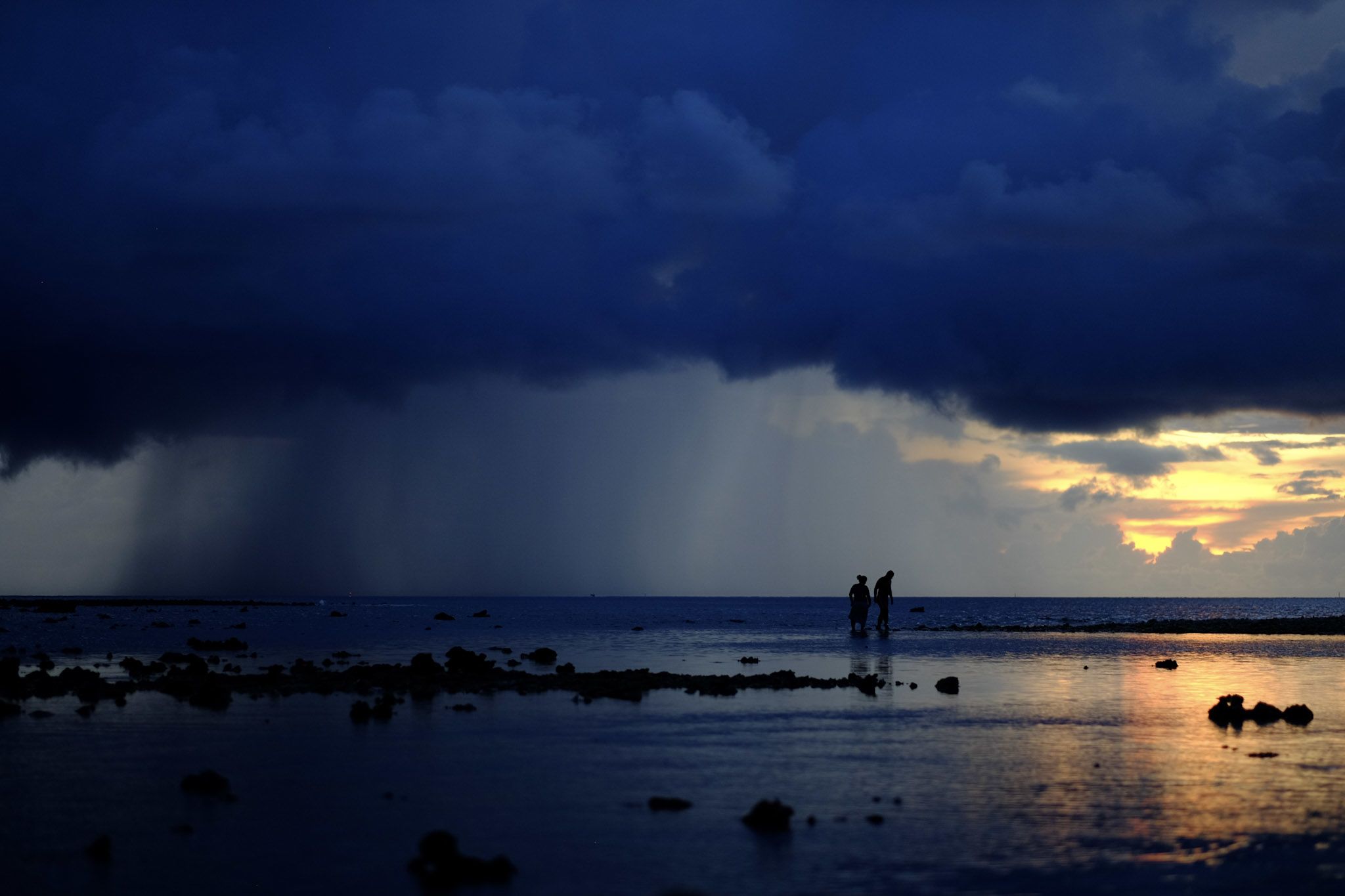 two figures on ocean edge with rainstorm approaching